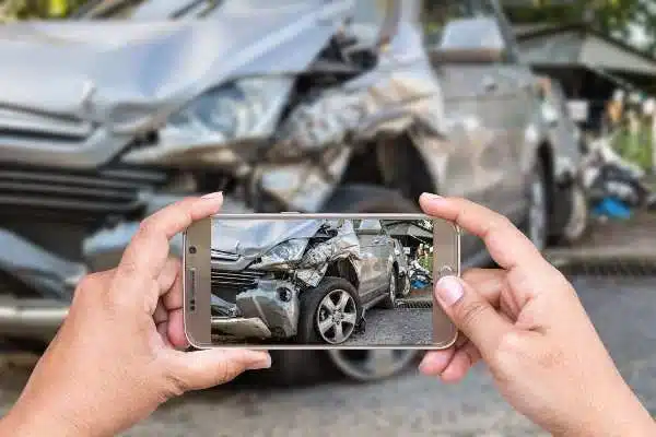 A person taking a photo of a damaged car, using a smart phone.
