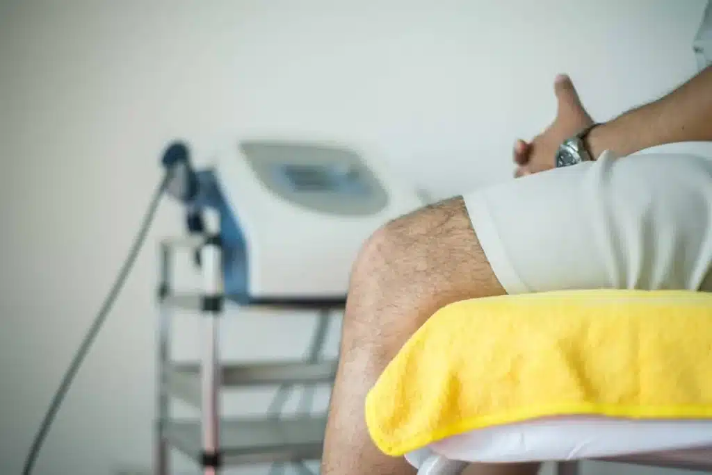 A patient wearing a medical gown, sitting on an exam table.