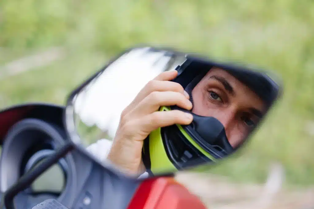 Motorcycle rider wearing a bright yellow helmet, looking in the rear view mirror.