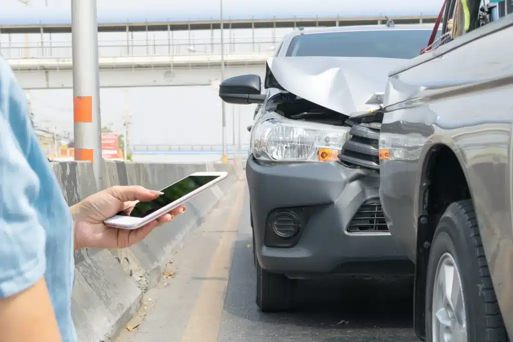 A car hitting the back of another car and someone standing in front of the accident on their phone.