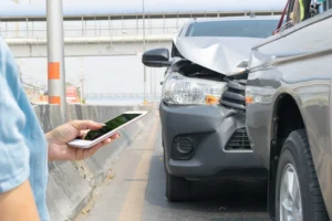 A car hitting the back of another car and someone standing in front of the accident on their phone.
