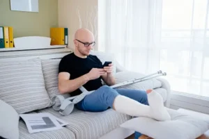 A man with a broken foot on the couch with his crutches.