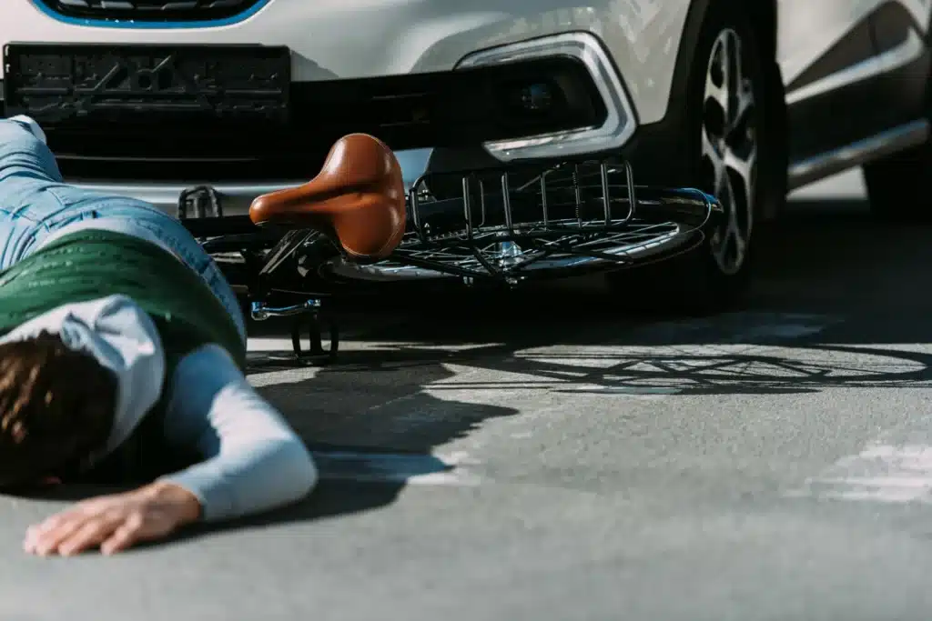 A cyclist laying on the ground after being hit by a car while riding his bike.